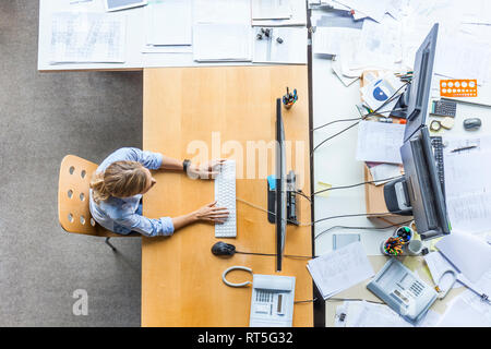 Blick von oben auf die Frau mit Computer am Schreibtisch im Büro durch Dokumente umgeben Stockfoto