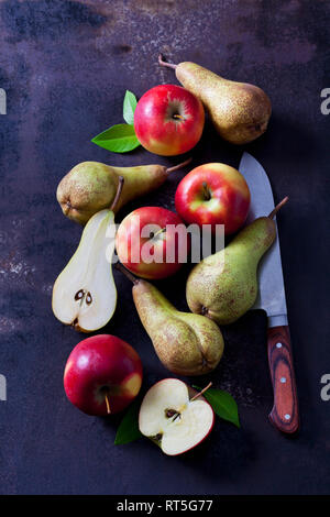 In Scheiben geschnitten und ganze Äpfel und Birnen auf dunklem Boden Stockfoto