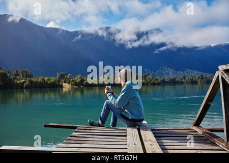 Chile Chaiten, Lago Rosselot, Frau sitzt auf der Jetty holding Becher Stockfoto