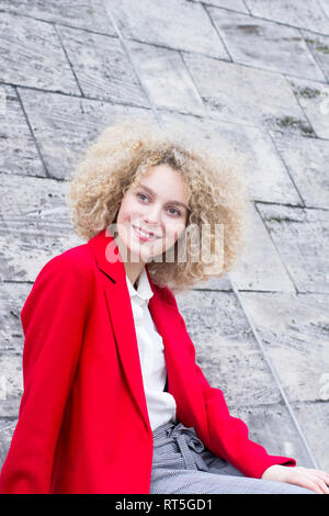 Portrait von lächelnden blonde Frau mit korkenzieherlocken das Tragen der roten Mantel Stockfoto