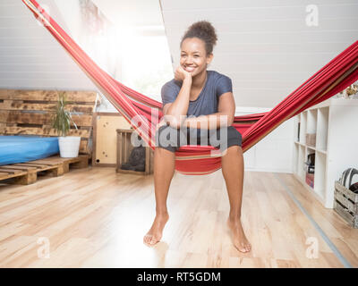 Porträt der glückliche junge Frau, die in einer Hängematte sitzen Stockfoto