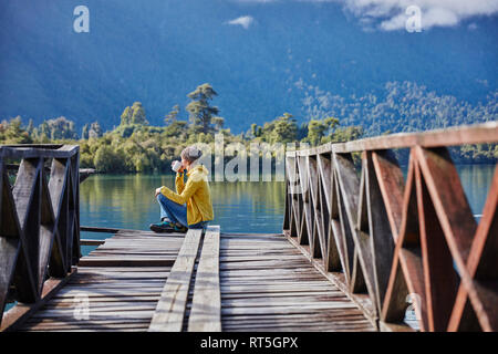 Chile Chaiten, Lago Rosselot, Frau sitzt auf der Jetty das Trinken aus Becher Stockfoto