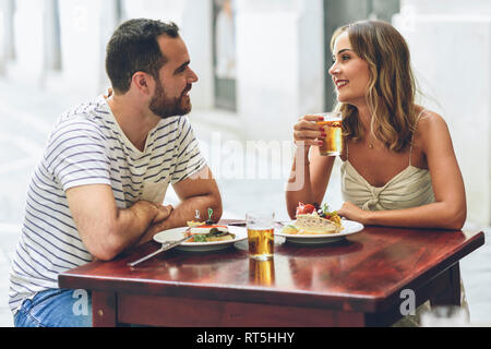 Lächelndes Paar essen und trinken Bier in einem Restaurant auf der anderen Straßenseite Stockfoto