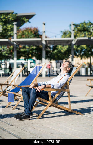 Reifer Mann relaxen im Liegestuhl auf einem Platz in der Stadt Stockfoto
