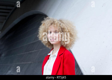 Portrait von lächelnden blonde Frau mit korkenzieherlocken das Tragen der roten Anzug Mantel Stockfoto