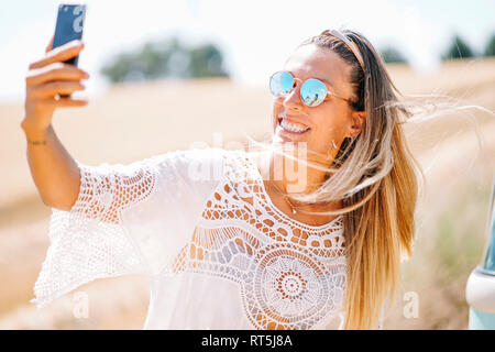 Porträt der blonde junge Frau mit verspiegelten Sonnenbrillen unter selfie mit Smartphone Stockfoto