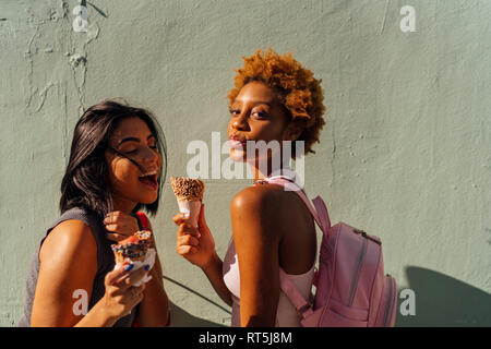 Zwei glückliche weibliche Freunde mit Eistüten an eine Wand stellen Stockfoto