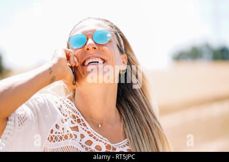 Lachend blonde junge Frau am Telefon mit verspiegelten Sonnenbrillen. Stockfoto