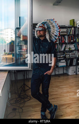 Mann mit indischen Kopfschmuck und VR-Brille in Büro, Blick aus Fenster Stockfoto