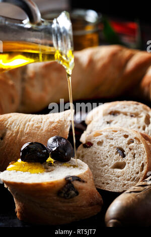 Gießen Olivenöl auf Scheibe Brot Ring mit schwarzen Oliven Stockfoto