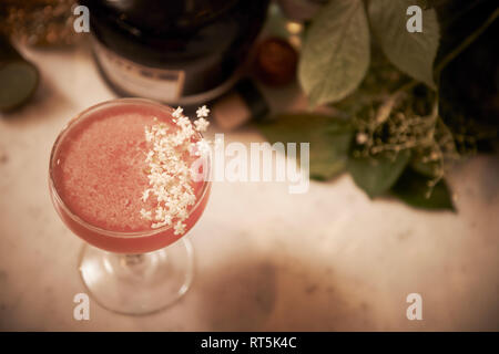 Eine gekühlte fruchtigen Cocktail mit einem weißen Blumen schmücken in der Nähe einer Flasche Schnaps und einige schöne Pflanzen bei einem atmosphärischen Weinbar. Stockfoto