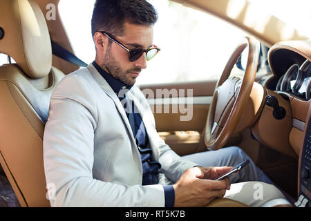 Junge Unternehmer im Auto sitzen, sie ihr Smartphone Stockfoto