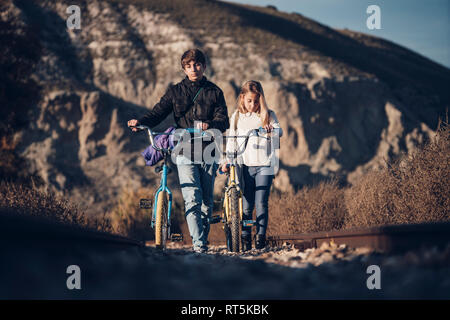 Junge und Mädchen zu Fuß auf der Bahn mit Fahrrädern Stockfoto