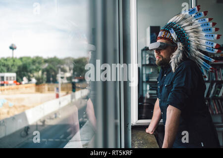 Mann mit indischen Kopfschmuck und VR-Brille in Büro, Blick aus Fenster Stockfoto