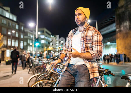 UK, London, Mann mit Fahrrad und Handy pendeln in der Nacht in der Stadt Stockfoto