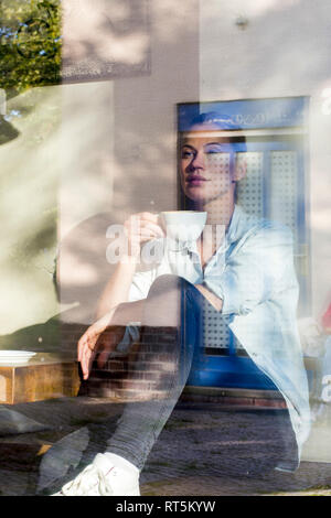Frau sitzt in einem Cafe trinken Tasse Kaffee, während Sie das Fenster Suchen Stockfoto
