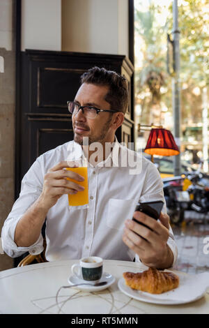 Geschäftsmann mit Frühstück in einem Cafe und Holding Handy Stockfoto