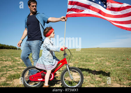 Mann und Tochter mit dem Fahrrad und die amerikanische Flagge auf dem Feld in abgelegenen Landschaft Stockfoto