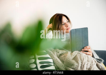 Frau sitzt auf der Couch, eingewickelt in eine Decke, Lesen von E-Books Stockfoto