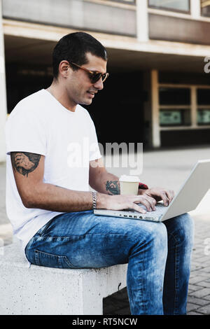 Junger Mann sitzt im Freien mit laptop Stockfoto