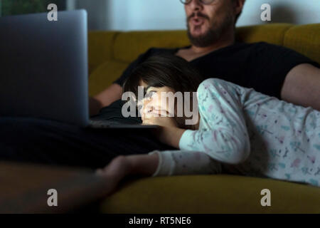 Glückliche Tochter und Vater am Laptop auf der Suche auf der Couch in der Nacht Stockfoto
