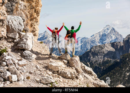 Italien, Cortina d'Ampezzo, Paar mit Seil und Kletterausrüstung bei Ansicht mit erhobenen Armen auf der Suche Stockfoto