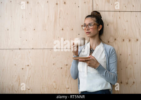 Junge Frau, die in kreativen Büro, Pause machen, Kaffee trinken aus Holz Schale Stockfoto