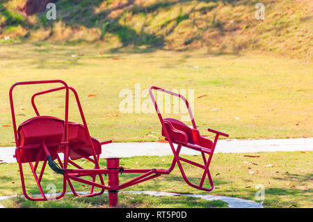 Eine wackelige Merry-go-round/Frohe Runde, hell in der Farbe Rot, liegend in Leer ein Kinderspielplatz. Stockfoto