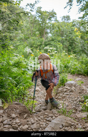 Ein junge Reisende mit einem Rucksack und Wanderstöcke klettert hinauf zu einer steilen Steigung Stockfoto