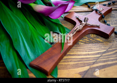 Kreuz mit Jesus Christus auf einem hölzernen Hintergrund mit einem violetten Calla und Rosenkranz-religiösen Ostern Fastenzeit Konzept Stockfoto