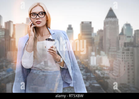 Sprechen über Vertrag... schöne junge Frau in der klassischen Verschleiß am Telefon zu sprechen und die Tasse Kaffee im Stehen im Freien mit Skyline im Hintergrund. Geschäftskonzept. Kommunikation. Kaffeepause Stockfoto