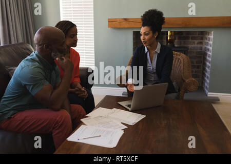 Weibliche real estate agent und Senior Paar diskutieren über Laptop im Wohnzimmer Stockfoto