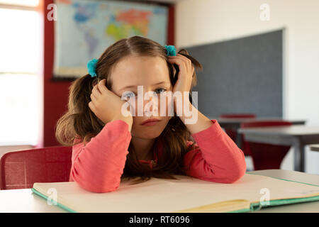 Trauriges Mädchen lehnte sich auf Schreibtisch in einem Klassenzimmer Stockfoto