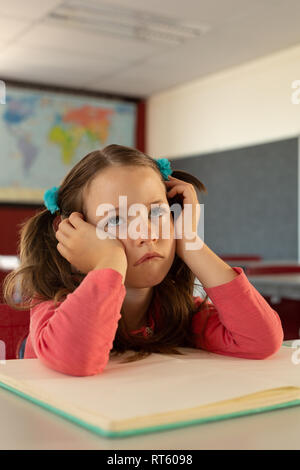 Trauriges Mädchen lehnte sich auf Schreibtisch in einem Klassenzimmer in der Schule Stockfoto
