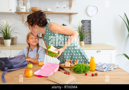 Schöne brünette Mutter und ihrer Tochter Verpackung gesundes Mittagessen und die Vorbereitung der Schultasche in der Küche Stockfoto