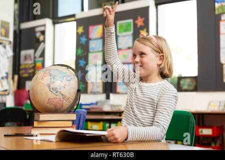 Schulmädchen heben ihre Hand an den Schreibtisch im Klassenzimmer Stockfoto