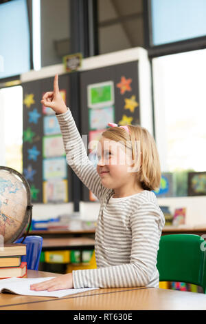 Schulmädchen heben ihre Hand an den Schreibtisch im Klassenzimmer Stockfoto