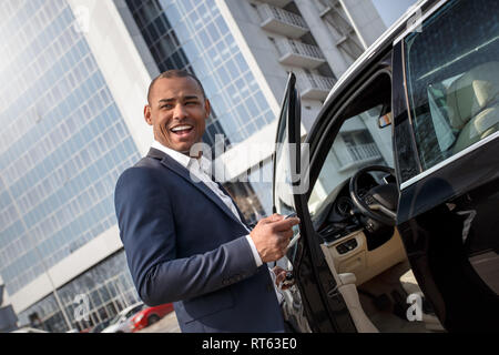 Junger Mann, der das Öffnen der Fahrzeugtür mit Alarm-Taste zur Seite schauen verspielten Stockfoto