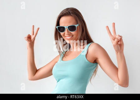 Freestyle. Frau in Sonnenbrille ständigen Studio isoliert auf weißem, friedenszeichen lächelt Fröhlich Stockfoto