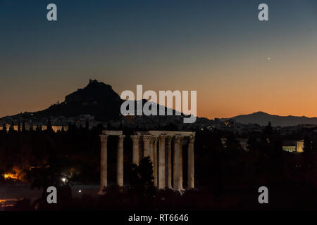 Die Ruinen der Tempel des Olympischen Zeus und den Berg Lycabettus mit Uhrturm und Agios Georgios bei Sonnenuntergang, Athen, Griechenland Stockfoto