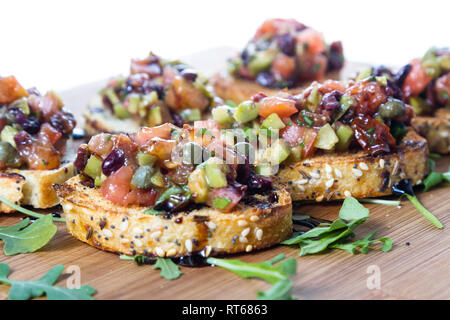 Frisches Bruschetta mit einer Vielzahl von Oliven und würfelt Tomaten auf kleinen getoasteten Brotscheiben mit Balsamico Reduzierung auf einer hölzernen Fach beträufelt gemacht Stockfoto