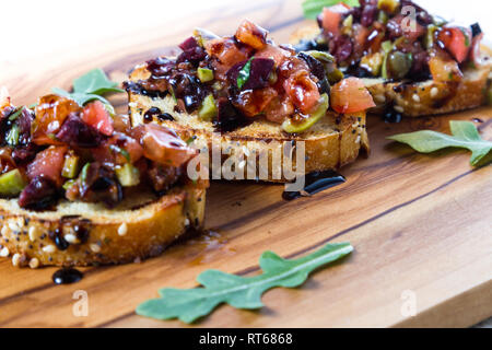 Frisches Bruschetta mit einer Vielzahl von Oliven und würfelt Tomaten auf kleinen getoasteten Brotscheiben mit Balsamico Reduzierung auf einer hölzernen Fach beträufelt gemacht Stockfoto