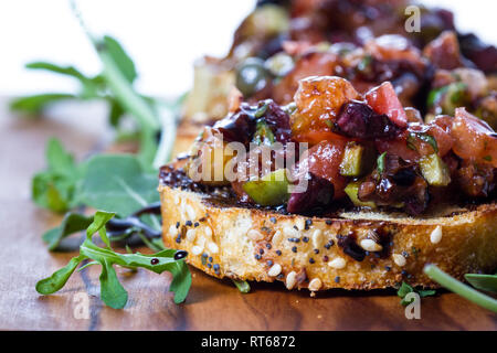 Frisches Bruschetta mit einer Vielzahl von Oliven und würfelt Tomaten auf kleinen getoasteten Brotscheiben mit Balsamico Reduzierung auf einer hölzernen Fach beträufelt gemacht Stockfoto