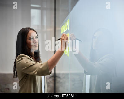 Geschäftsfrau schreiben auf Haftnotizen an der Glasscheibe im Büro Stockfoto