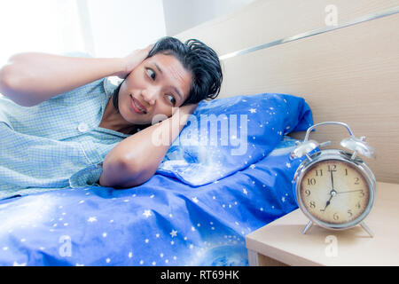 Eine Frau im Bett lag, hält und blockiert ihre Ohren beim Klingeln die Wecker. Unangenehm früh erwachen. Stockfoto