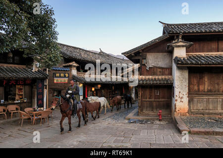 Shaxi, China - 21. Februar 2019: Pferde reiten im Zentrum von shaxi Altstadt in der Dämmerung Stockfoto