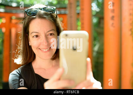 Frau verwendet Smart Phone zu fotografieren Torii Gates in Shinto Schrein Fushimi Inari-taisha, Kyoto, Japan. Fushimi Inari-taisha auf dem Berg Inari ist der Kopf Stockfoto