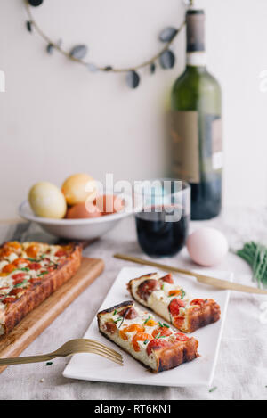 Hausgemachte Kuchen (quiche), mit Ricotta und frischen farbigen Tomaten, in Scheiben schneiden, in eine Schüssel mit goldenen Gabel schneiden, ein Glas Wein, rechteckigen Formen, frontal Stockfoto