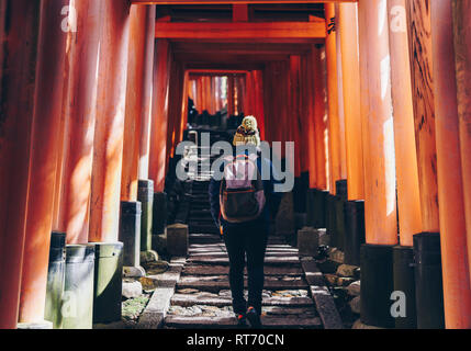 Frau Tourist mit Mütze zu Fuß die Treppe des Fushimi Inari Schrein in Kyoto als warmer Winter Sonne leuchtet durch die Tore. Stockfoto