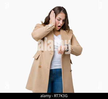 Schöne Übergrößen junge Frau tragen Winter Mantel über isolierte Hintergrund ein Blick auf die Uhr Zeit Sorgen, Angst, sich spät Stockfoto